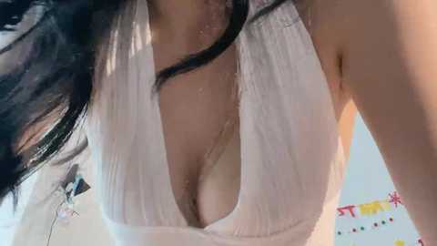 Video of a light-skinned woman with long black hair, wearing a wet, white, plunging neckline top that reveals ample cleavage, captured from a low angle.