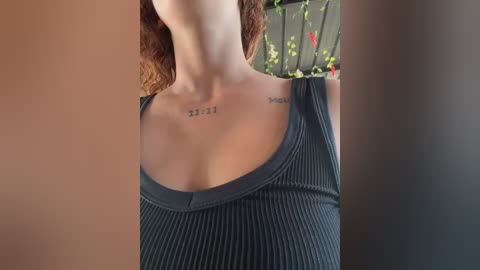 Video of a woman with shoulder-length, curly red hair, wearing a dark green ribbed tank top, showcasing two small tattoos with Roman numerals \"XIII\" on her collarbones.