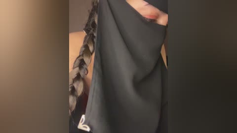 A close-up video of a person wearing a black jacket with a textured, braided design on the sleeves, standing against a plain beige wall. The jacket appears smooth and has a slight sheen.