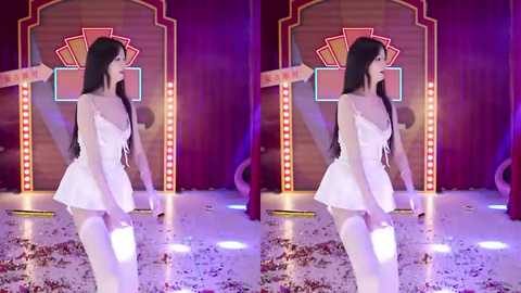 Video of an Asian woman with long black hair, in a white strapless dress, kneeling on a shiny floor with scattered rose petals. She's in a stage setting with a colorful, triangular backdrop and neon lights.