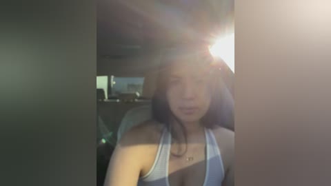 Media: A video of a young woman with long brown hair, wearing a white tank top, seated in a dimly lit car, her face partially obscured by sunlight.