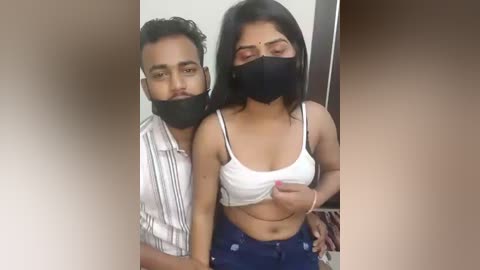 Video of two South Asian individuals, a man and woman, wearing black face masks, with the woman lifting her white crop top to expose her cleavage.