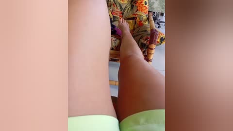 A video showing a close-up of a person's tan legs in light green socks, with a colorful, floral-patterned cushioned chair in the background.