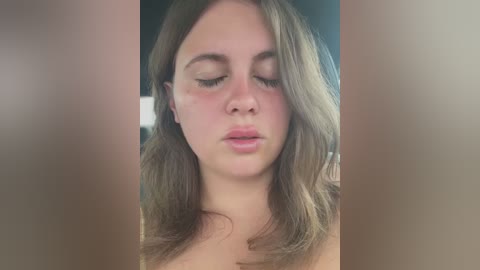 Video of a young Caucasian woman with fair skin and shoulder-length brown hair, eyes closed, lips slightly parted, appearing emotional, possibly crying, with blurred, dark background.