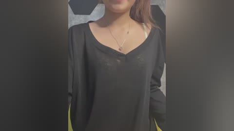 Video of a woman wearing a black, long-sleeved, V-neck shirt with yellow sleeves. She has light brown skin and her face is partially out of frame. Background features a soccer ball and blurred text.