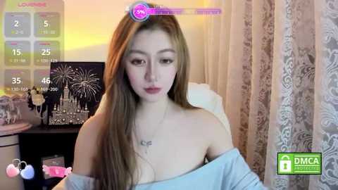 Video of a young East Asian woman with long, light brown hair, wearing a light blue off-shoulder top, sitting in a dimly lit room with a TV showing a countdown timer, and a decorative cityscape poster.