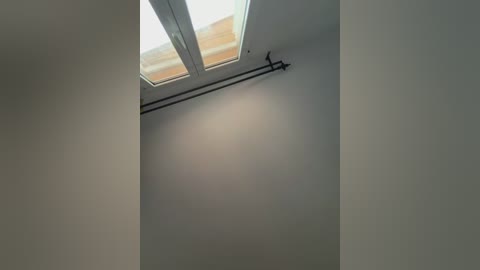 Media: A video of a minimalist attic space with a white ceiling and a black metal rod hanging from the corner. A small window with frosted glass allows natural light to illuminate the area.