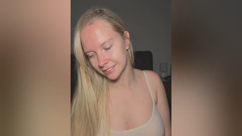 Video of a smiling, fair-skinned, blonde woman in a light-colored tank top, leaning forward with her eyes closed, slightly blurred background.