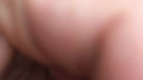 The image is a blurred video showing the close-up of a person's pale skin with visible pores, likely taken in a natural light setting. The focus is on the skin texture, making facial features indiscernible.