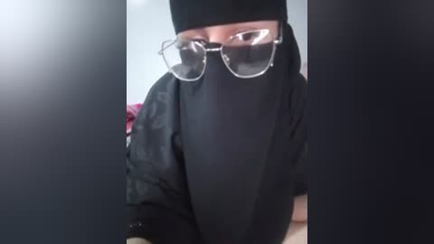 Video of a person wearing a black face mask, black hoodie, and large glasses, with blurred background.