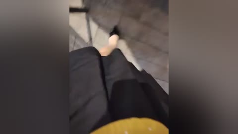 Video of a person's legs in black pants and yellow socks, walking on a tiled floor with a gray pattern. The image is slightly blurred and out of focus.