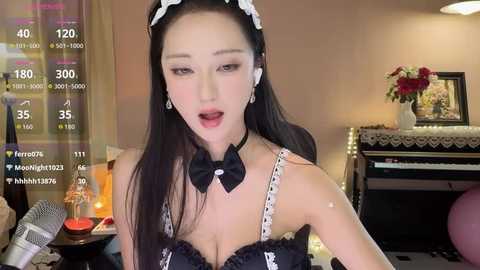 Video of an East Asian woman with long black hair, fair skin, and light makeup, wearing a black and white maid outfit with a bow tie, sitting on a piano in a cozy, dimly-lit room.