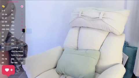 Video of a modern, cream-colored leather recliner with a light green pillow, positioned against a white wall. A person, wearing a gray hoodie, stands in the background.