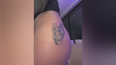 A video of a person's upper thigh featuring a detailed, black ink tattoo of a face with intricate lines and shading, partially visible in dimly lit indoor setting.