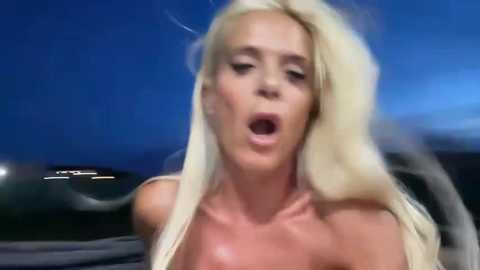Video of a blonde woman with long, flowing hair, open-mouthed in apparent pleasure, against a dark sky background.