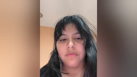 A video of a young Asian woman with long black hair, wearing a black top, standing in a room with beige walls and a white ceiling.