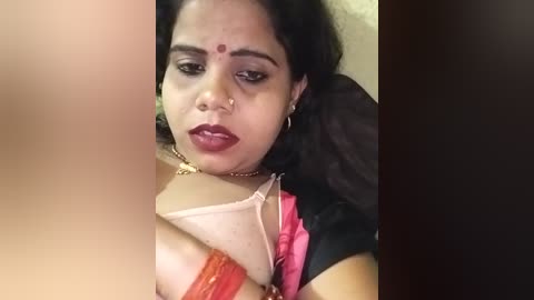Media: Video of a dark-skinned woman with a medium build, wearing a red blouse and a pink bra, her face marked with a red bindi and a nose ring. She appears emotional or distressed.