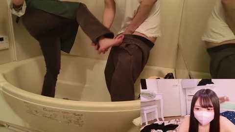 Video: A man in a green shirt and black pants adjusts the pants of another man in a beige shirt, both in a bathtub. A third person, a woman in a white mask, sits on a bed in the background.