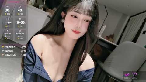 Media: A video of an Asian woman with long black hair, wearing an off-shoulder blue dress, in a modern, minimalist living room.