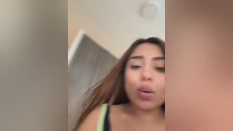 Media: A blurred, candid video of a young woman with long brown hair, wearing a black top, with a neutral background.