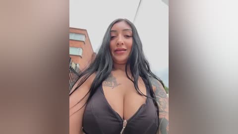 Video of a curvy, tattooed Latina woman with long black hair, wearing a black halter top, standing outside a building.