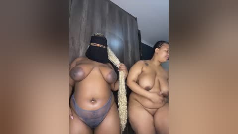 Video of two nude women with different skin tones and body types, standing in a dimly lit room, one holding a long rope, wearing a black mask.