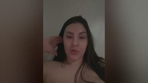 Media: A video of a young, topless Asian woman with long black hair, fair skin, and full lips, reclining against a neutral-colored wall, with her right hand in her hair.