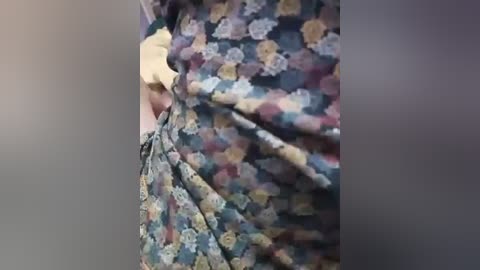 Media: A video showing a person's lower torso and legs in a floral-patterned dress. The dress features a mix of blue, yellow, and green hues, with a slightly textured fabric. The background is blurred, emphasizing the dress.
