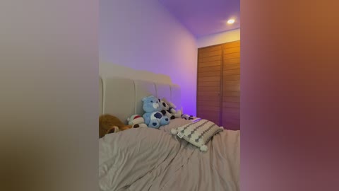 Media: A video of a cozy bedroom with a plush, white upholstered headboard, a light grey bedspread, and a blue stuffed bear. Soft, warm lighting creates a calming ambiance.