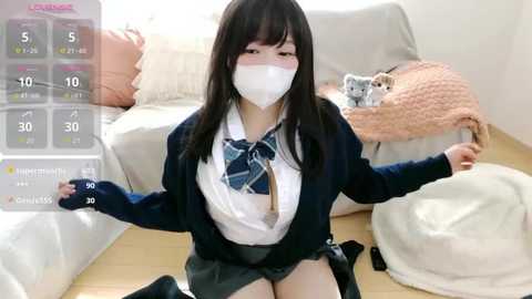 Video of an Asian woman with long black hair, wearing a school uniform, mask, and gloves, holding a remote, sitting on a beige couch, surrounded by a virtual reality interface.