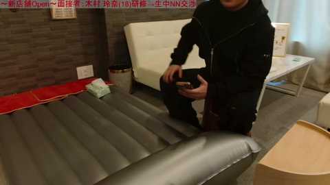 Video of a man in a black hoodie and jeans assembling a white leather bed frame in a modern room with gray tiled walls.