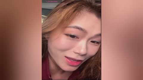 Media: Video of a close-up, smiling Asian woman with light skin, wearing pink lipstick, and brown hair, partially obscured by two brown hands.