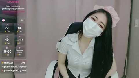 Video of an Asian woman in a white maid outfit, with a pink bow, face mask, and long black hair, sitting on a chair, surrounded by virtual reality gaming elements.