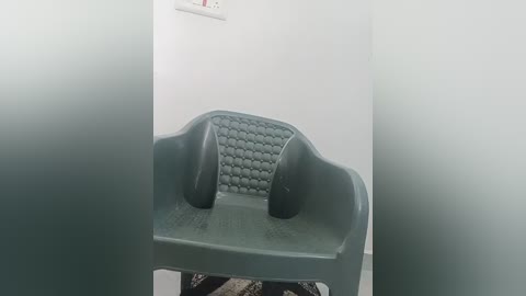 Media: Video of a green plastic chair with a textured backrest, partially obscured by frosted glass, against a white wall, with a power outlet visible.