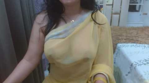 Media: Video of a South Asian woman with medium skin tone, wearing a sheer yellow sari, exposing her medium-sized breasts, in a room with a white table and a woven basket.