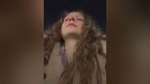 Media: A close-up video of a woman with long, wavy brown hair, pale skin, and closed eyes, possibly in ecstasy or deep thought, set against a dark background, blurred edges suggesting a dreamy or introspective state.