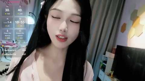 A video of a young Asian woman with long black hair, fair skin, and closed eyes, wearing a pink top, indoors with a virtual reality headset.