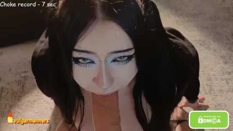 A video of a woman with long black hair and striking blue eyes, wearing heavy makeup, performing oral sex on an erect penis, with a watermark and timestamp visible.