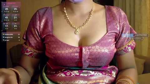 Video of a South Asian woman with medium brown skin, wearing a pink, gold-embroidered blouse, gold necklace, and bracelets. Background shows a dimly lit room with a \"Live\" status on the left side.