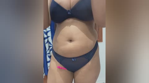 A video of a woman in a navy blue lace lingerie set, standing in a bathroom with a blue and white patterned shower curtain and wooden door background.