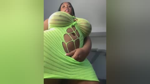 Video of a plus-sized Black woman with a voluptuous figure, wearing a neon green, sheer, cut-out dress. She has medium brown skin, long black hair, and a confident expression. Background is a minimalist, modern room with white walls and a gray ceiling.