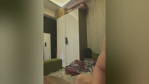 A video captures a cluttered bedroom with a person's legs visible, wearing red and white striped socks. The room has a green couch, white wardrobe, and a messy bed with a red blanket.