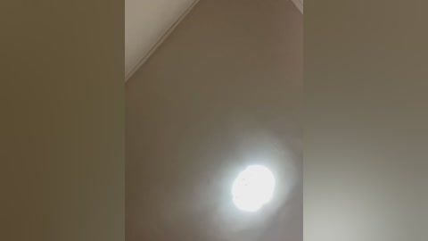 Video of a ceiling light emitting a bright, circular glow against a muted beige background. The image is slightly blurred, with soft lighting and a minimalist, modern aesthetic.