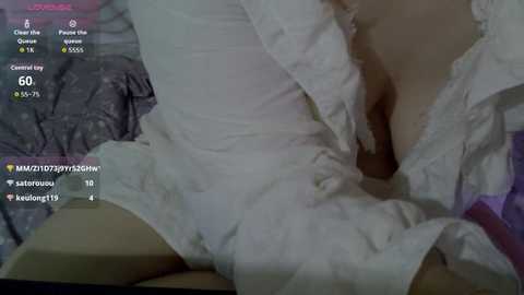Media: Video of a partially clothed person lying on a bed, with a white shirt partially unbuttoned, revealing a glimpse of cleavage, and a grey shirt underneath. The image includes digital overlays of a YouTube video player and chat, indicating a live stream.