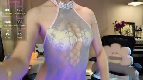 Media: Video of a light-skinned person wearing a sheer, lavender lace bodysuit with a halter neckline, revealing a partially transparent, patterned bra underneath. Background includes a gaming chair, desk, and digital fitness stats overlay.