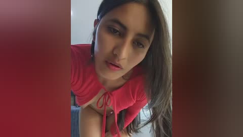 Video of a young woman with long dark hair, wearing a red crop top, leaning forward with a sultry expression, partially obscured by red and brown vertical bars.