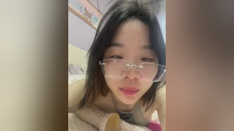 Media: Video of an Asian woman with shoulder-length black hair, wearing clear-framed glasses, lying on a bed in a cozy bedroom setting.