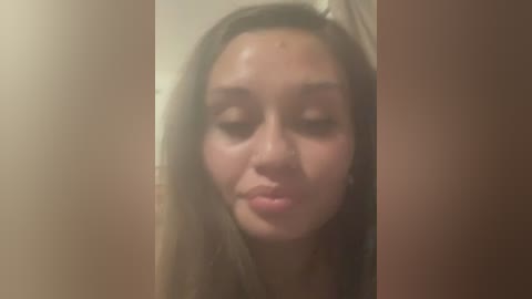 Video of a young woman with long brown hair, light skin, and closed eyes, leaning against a brown door, with a blurry, out-of-focus background.