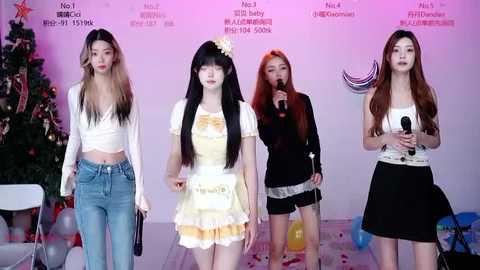 Video of four East Asian women in different outfits, singing on a stage with Christmas decorations.