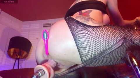 Video of a curvy woman with tattoos, wearing black fishnet stockings, riding a vintage scooter indoors; red wall and retro lamp in background.